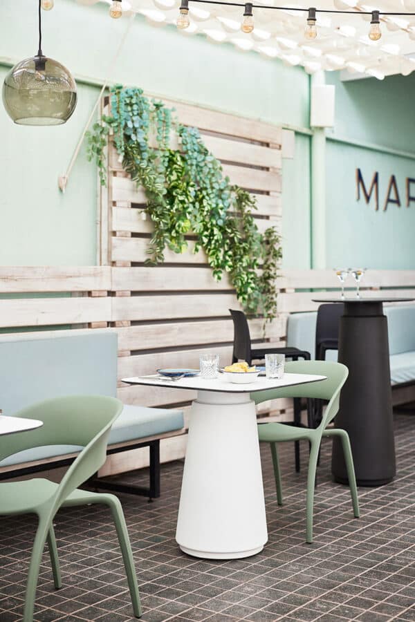Dorik Cafe Table in a stylish outdoor café setting with a round tabletop and pedestal base